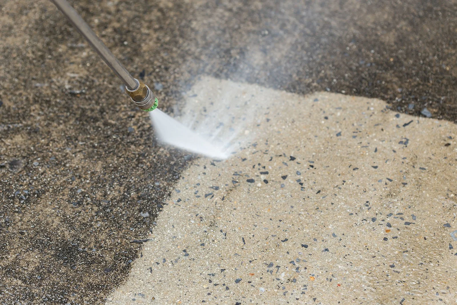 Professional pressure washing cleaning grime from a concrete surface.