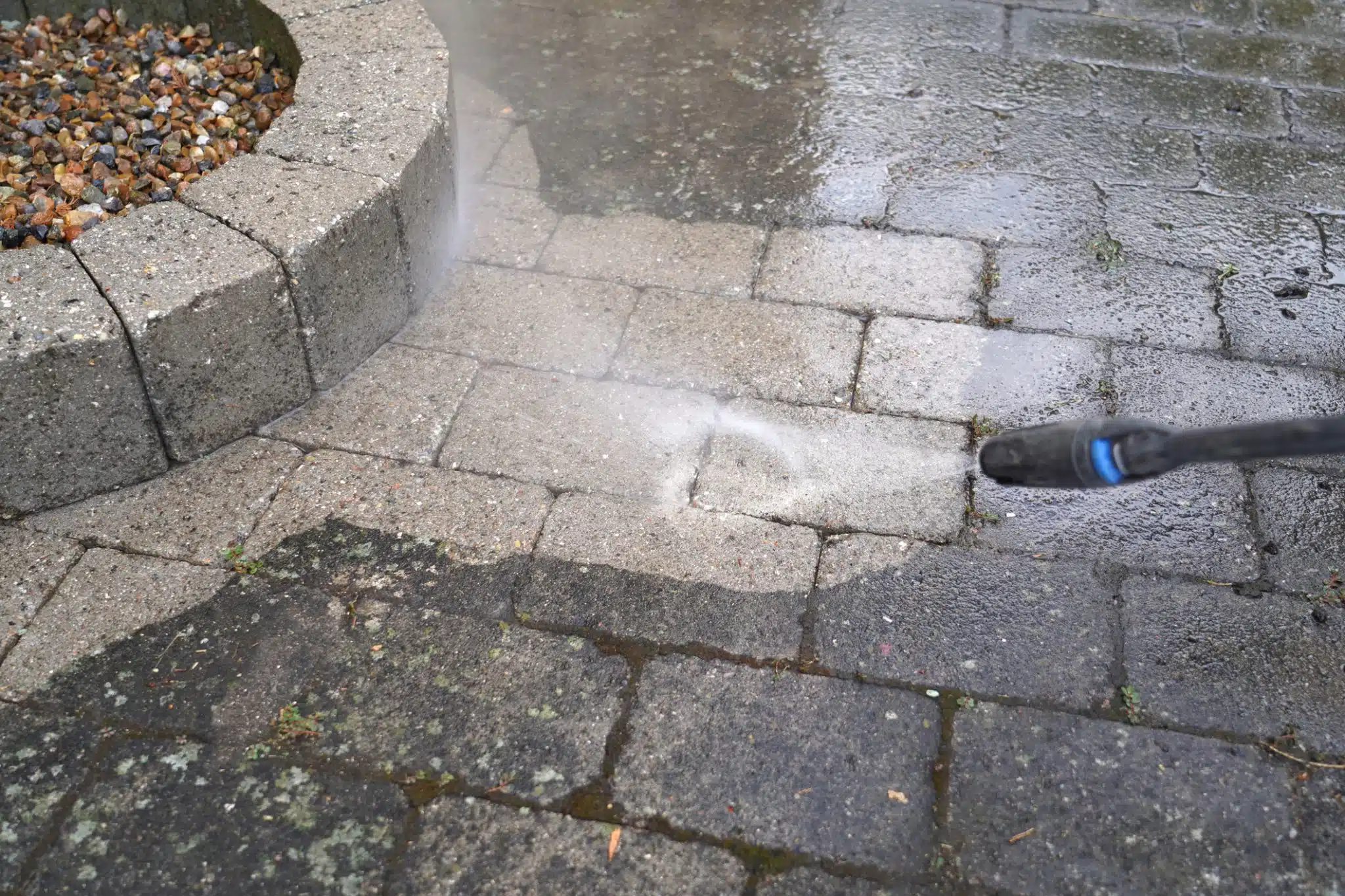Pressure washing a dirty paver patio to remove moss, algae, and built-up grime.
