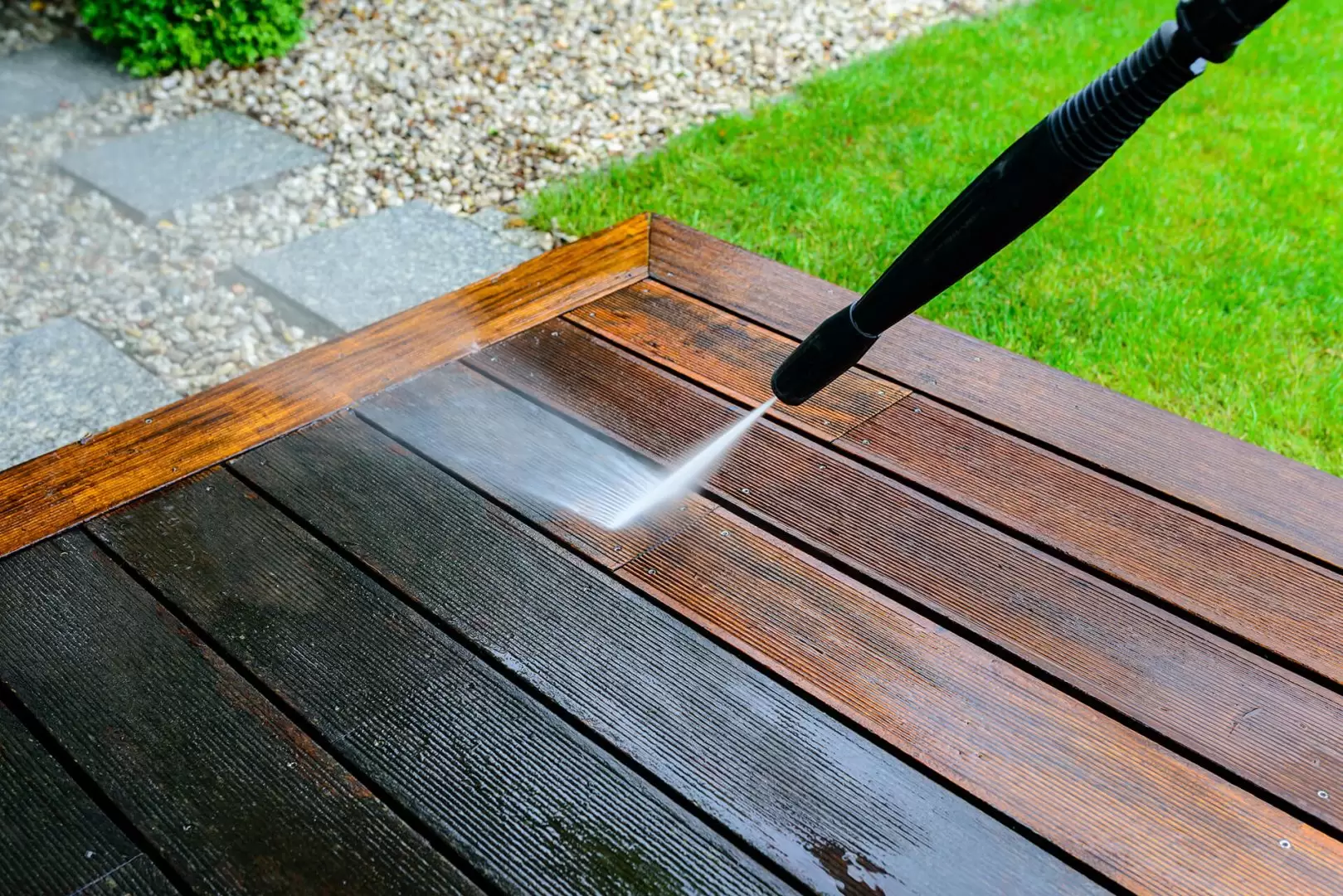Soft washing a wood deck surface with water spray during outdoor deck cleaning.