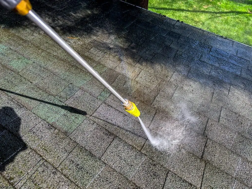 Soft washer cleaning moss and grime from asphalt roof shingles.